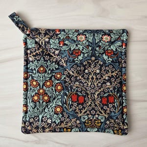 May include: Square pot holder with a floral pattern in shades of navy, teal, orange, and white. The design features stylized flowers and foliage. A fabric loop is attached for hanging. Kitchen and dining decor.