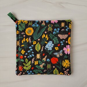 May include: Black pot holder with a floral pattern featuring butterflies, ladybugs, and flowers in shades of red, yellow, green, blue, and pink.