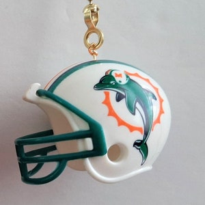 May include: A white football helmet with a green face mask and a Miami Dolphins logo. The helmet is attached to a gold chain.