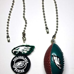 May include: Two fan pull chains with Philadelphia Eagles logos. One chain has a green and white logo and a black and white logo. The other chain has a football-shaped pull with a green and brown design and a white logo.