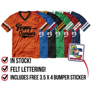 May include: Six different color t-shirts with a black felt "Happy Camper" graphic. The t-shirts have a v-neck and striped sleeves. A free 3.5 x 4 inch bumper sticker is included.