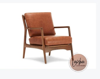 Op de afbeelding: Een bruine leren fauteuil met een houten frame. De stoel heeft een mid-century modern design met afgeschuinde poten en armleuningen.