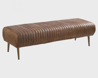 May include: A brown, rectangular bench with a vertically ribbed design. The bench has rounded ends and sits on four thin, gold-colored legs. The overall design is modern and stylish, suitable for various interior settings.