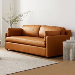 May include: A brown leather sofa with a tufted back and two cushions. The sofa is sitting on a white rug in a room with white walls.