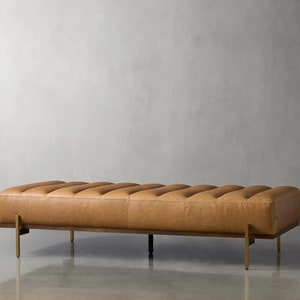 May include: A long, rectangular brown leather bench with a tufted design and gold metal legs.