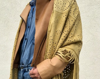 May include: A tan suede shawl with fringe and cut-out designs. The shawl is worn over a brown leather jacket and blue jeans.
