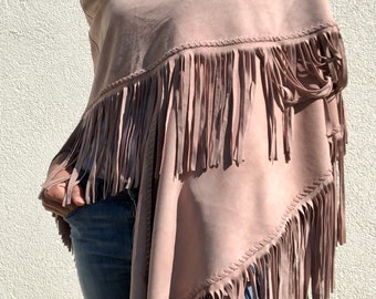 May include: A dusty rose coloured poncho made of a soft, suede-like material. The garment features a draped neckline and long, vertical fringe detailing along the edges, which are finished with a decorative whipstitch pattern throughout the piece.