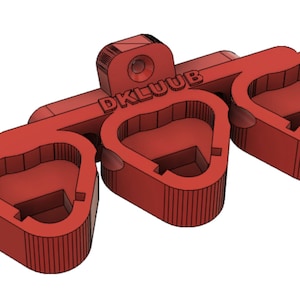 May include: A red plastic object with three heart-shaped openings, connected by a bar. The text "DKLUUB" is printed on the bar. The object has a hole on the top. The object is likely a tool or a part of a larger device.