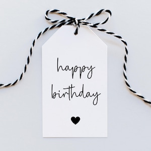 Puede incluir: Etiqueta de regalo blanca con una cuerda negra atada en un lazo. La etiqueta tiene el texto "feliz cumplea&ntilde;os" escrito en cursiva negra y un peque&ntilde;o coraz&oacute;n negro.