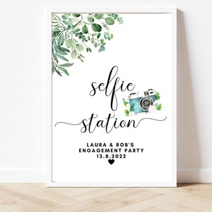Puede incluir: Un cartel imprimible con una ilustraci&oacute;n de acuarela de vegetaci&oacute;n y una c&aacute;mara vintage. El texto dice "selfie station" con las palabras "Laura & Rob's Engagement Party 13.8.2022" debajo.