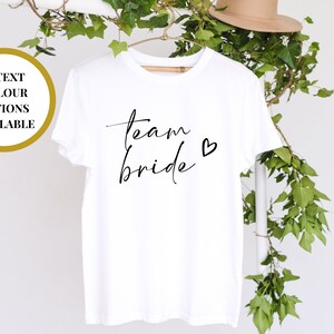 Puede incluir: Camiseta blanca con texto negro que dice "team bride" con un pequeño corazón.