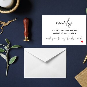 Op de afbeelding: Een witte kaart met zwarte tekst die "emily I CAN'T MARRY MY MR WITHOUT MY SISTER. will you be my bridesmaid?" zegt met een klein rood hartje.