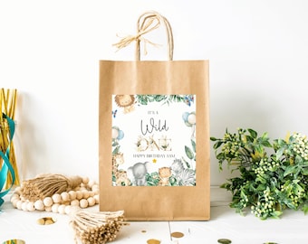 May include: A brown paper gift bag with a decorative label that reads "It's a Wild One" with jungle animal illustrations. The bag has a twisted paper handle and is decorated with a raffia bow.