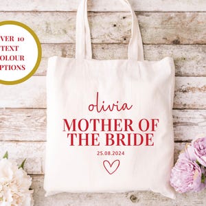 Puede incluir: Bolsa de tela blanca con texto rojo que dice "Olivia Madre de la Novia 25.08.2024" con un pequeño corazón rojo.