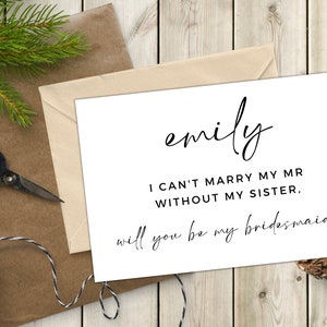 Op de afbeelding: Een witte kaart met zwarte tekst die "emily I CAN'T MARRY MY MR WITHOUT MY SISTER. will you be my bridesmaid?" zegt met een klein rood hartje.