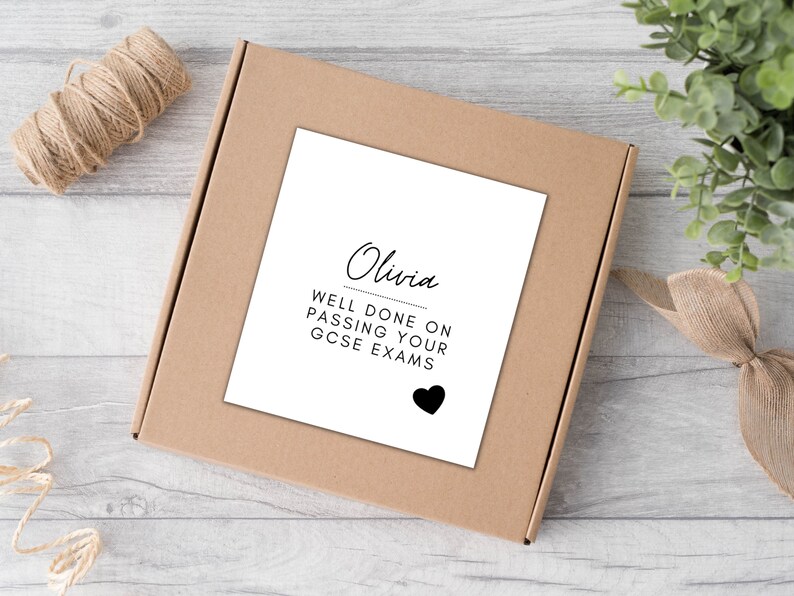 Puede incluir: Una caja de cart&oacute;n marr&oacute;n con una tarjeta blanca. La tarjeta dice "Olivia, BIEN HECHO AL APROBAR TUS EX&Aacute;MENES GCSE" con un coraz&oacute;n negro. Tambi&eacute;n se ven hilo y vegetaci&oacute;n.