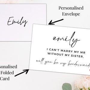 Op de afbeelding: Een witte gevouwen kaart met zwarte tekst die "emily I CAN'T MARRY MY MR WITHOUT MY SISTER, will you be my bridesmaid?" luidt, met een klein rood hart. De kaart is aan de voorkant geadresseerd aan "Emily".