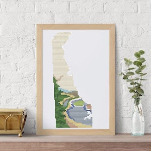 Könnte beinhalten: Eine Kreuzstich-Stickerei des Bundesstaates Delaware, mit einer grünen und braunen Landschaft und einem blauen Gewässer. Die Stickerei ist in einem hellen Holzrahmen gerahmt.