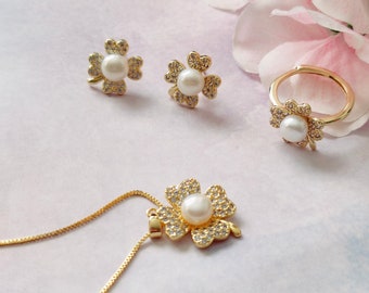 May include: A gold clover necklace, ring, and earrings set with a pearl in the center of each clover. The jewelry is on a white background.