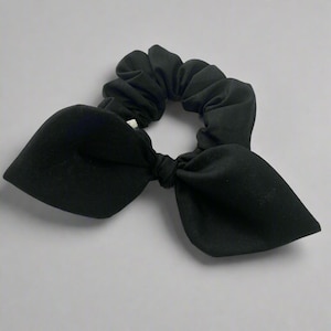 May include: A black scrunchie with a bow. The scrunchie is made of a soft, stretchy fabric.