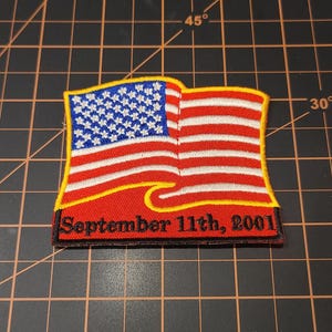 May include: A red, white, and blue American flag patch with a yellow wave design and the text "September 11th, 2001".