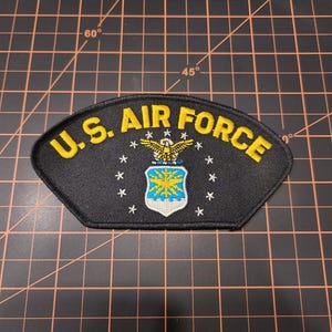 May include: A black embroidered patch with the words "U.S. AIR FORCE" in yellow lettering. The patch features a blue and yellow shield with a white eagle and stars.