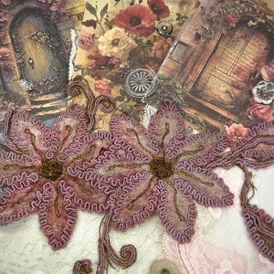 May include: Close-up of two large, pink floral appliques with gold thread detailing. The appliques are placed on a background of vintage-style floral cards, lace, and decorative buttons. The overall aesthetic is romantic and vintage.