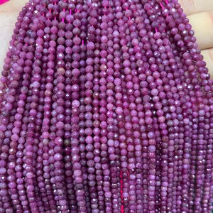 Pode incluir: Um fio de contas de rubi, facetadas e redondas, de cor rosa intenso. As contas são enfiadas em um fio fino e estão dispostas em um padrão ordenado e paralelo.