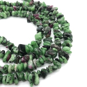 Op de afbeelding: Een streng groene, zwarte en roze edelsteenchips. De chips zijn onregelmatig gevormd en hebben een natuurlijke, ruwe textuur.
