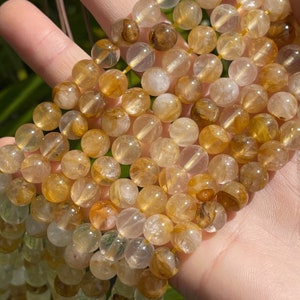 May include: A strand of round, translucent golden rutilated quartz beads. The beads have a light golden color with brown inclusions.