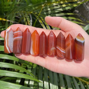 May include: Ten carnelian crystal points with a pointed tip and a smooth, polished finish. The crystals are a mix of red, orange, and white colours.