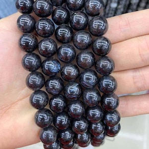 Puede incluir: Una hebra de cuentas de piedras preciosas negras con un efecto brillante e iridiscente. Las cuentas son redondas y lisas, y están enhebradas en un cordón elástico transparente.