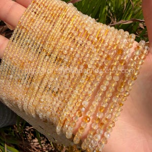 Puede incluir: Primer plano de múltiples hebras de pequeñas cuentas facetadas de color amarillo dorado. Las cuentas están ensartadas, creando un efecto brillante. La imagen está bien iluminada, resaltando el color y la textura de las cuentas. El texto "https://prettybeadstrands.etsy.com" es visible.