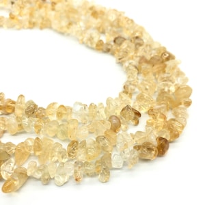 Pode incluir: Um fio de contas de pedra preciosa em forma de lascas de cor amarelo claro e âmbar. As contas são de forma irregular e têm um acabamento natural e polido.