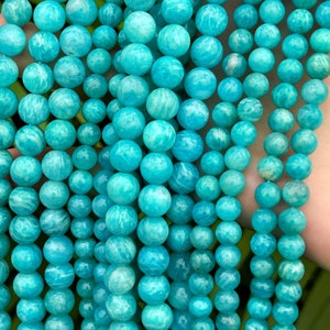 May include: A strand of teal blue amazonite beads. The beads are round and smooth, with a slightly translucent finish.