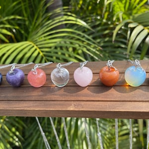 Pode incluir: Um conjunto de oito pingentes de maçã de cristal em correntes de prata. Os pingentes são feitos de várias pedras preciosas, incluindo ametista, quartzo rosa, quartzo transparente e sodalita.