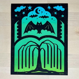 May include: A black and green print featuring a bat, clouds, stars, and a tree. The bat is in the center, with a crescent moon above. The tree is at the bottom, with a gradient of green. The sky is black with blue clouds and stars.