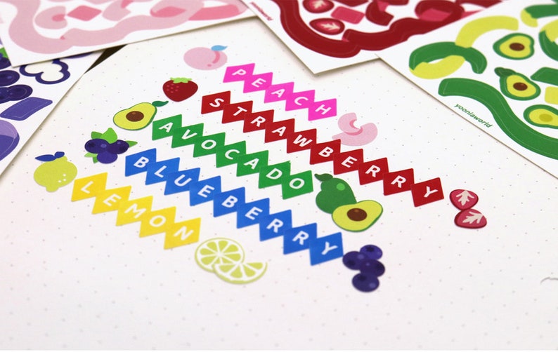 May include: A set of colorful fruit and vegetable stickers with the names of each fruit or vegetable written on them. The stickers are arranged in a rainbow pattern, with the colors of the rainbow corresponding to the colors of the fruits and vegetables. The stickers are on a white background with small white dots.