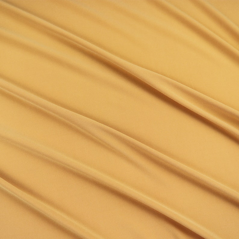 May include: A smooth, golden yellow fabric with soft, flowing folds. The fabric has a subtle sheen and a luxurious feel.