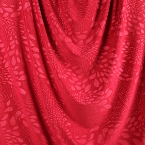 May include: Red fabric with a swirling pattern of pink and white teardrop shapes.