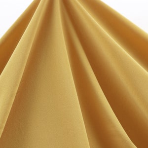 May include: A close-up of a smooth, golden yellow fabric with a subtle texture. The fabric is draped and folded, creating soft, flowing lines.