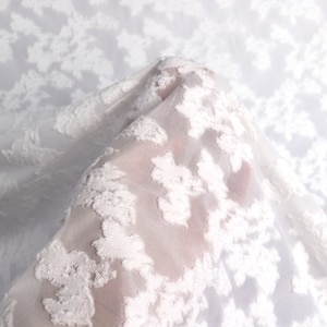 May include: White sheer fabric with an embossed floral pattern. The fabric is delicate and has a soft, flowing texture.