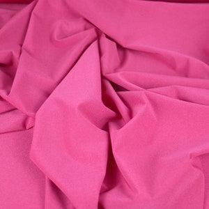 May include: Close-up of a pink fabric with a smooth, silky texture. The fabric is folded and draped, creating soft, flowing lines.
