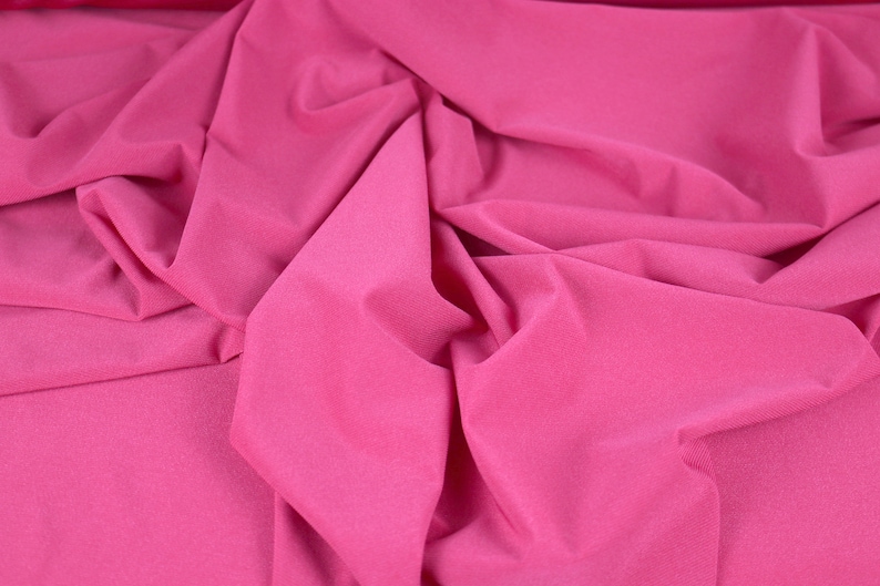 May include: Close-up of a pink fabric with a smooth, silky texture. The fabric is folded and draped, creating soft, flowing lines.