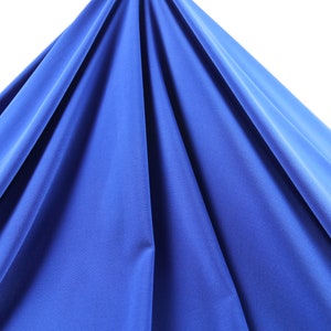 May include: A close-up of a smooth, royal blue fabric draped over a white surface. The fabric is soft and has a slight sheen.