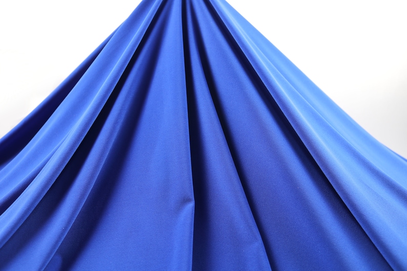 May include: A close-up of a smooth, royal blue fabric draped over a white surface. The fabric is soft and has a slight sheen.