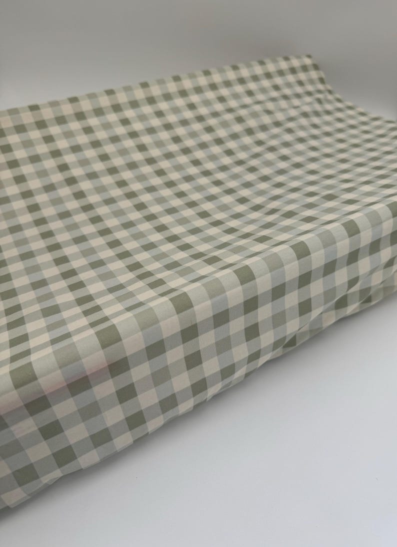 May include: A green and white gingham fabric with a subtle sheen. The fabric is folded and appears to be soft and lightweight.