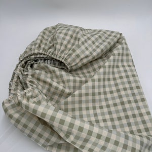 May include: A green and white gingham fitted sheet. The sheet is folded and crumpled, showing the fabric texture.