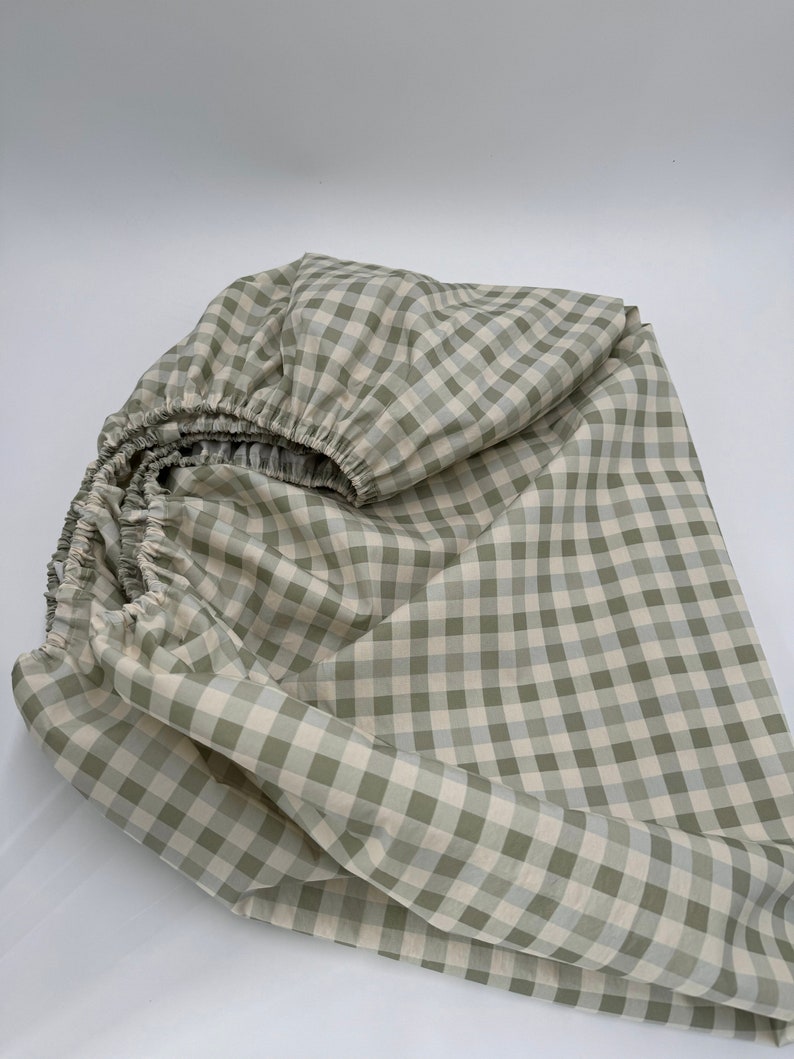 May include: A green and white gingham fitted sheet. The sheet is folded and crumpled, showing the fabric texture.