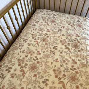 May include: A cream-colored fitted crib sheet with a brown floral pattern. The sheet is made of a soft, breathable fabric and is perfect for a nursery.